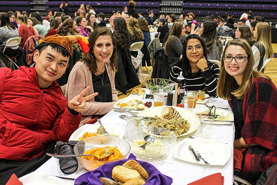 Photo of international students at a Chatham University harvest dinner, smiling for the camera as they eat dinner