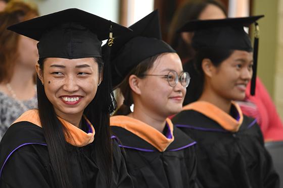 Photo of three Chatham University international students at graduation in caps and gowns