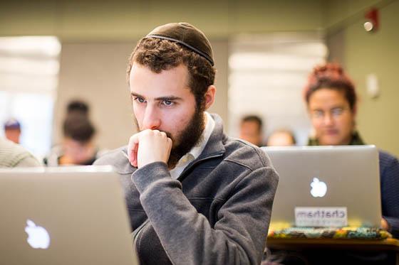 Photo of a male student in a yarmulke, sitting in a Chatham University lecture hall and looking at his computer