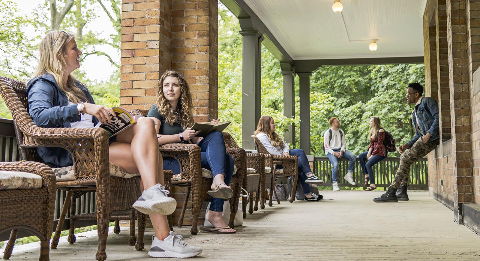 Photo of Chatham University students on a porch on Shadyside Campus, talking together and studying