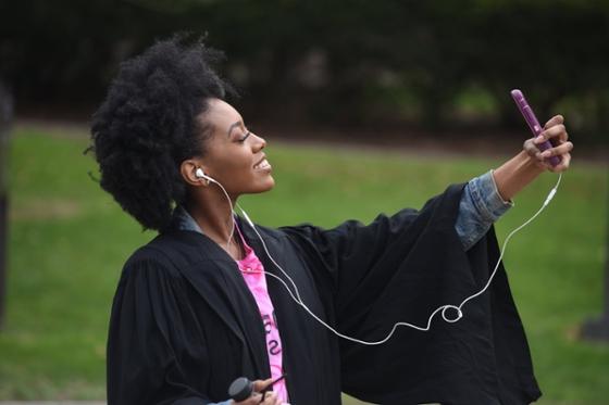 Photo of a female Chatham University student in graduation robes, taking a selfie and smiling