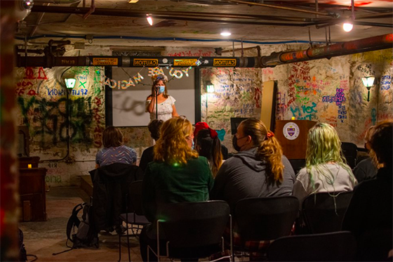 Photo of an event in Rea Coffeehouse, with students seated facing a stage with a person speaking into a microphone