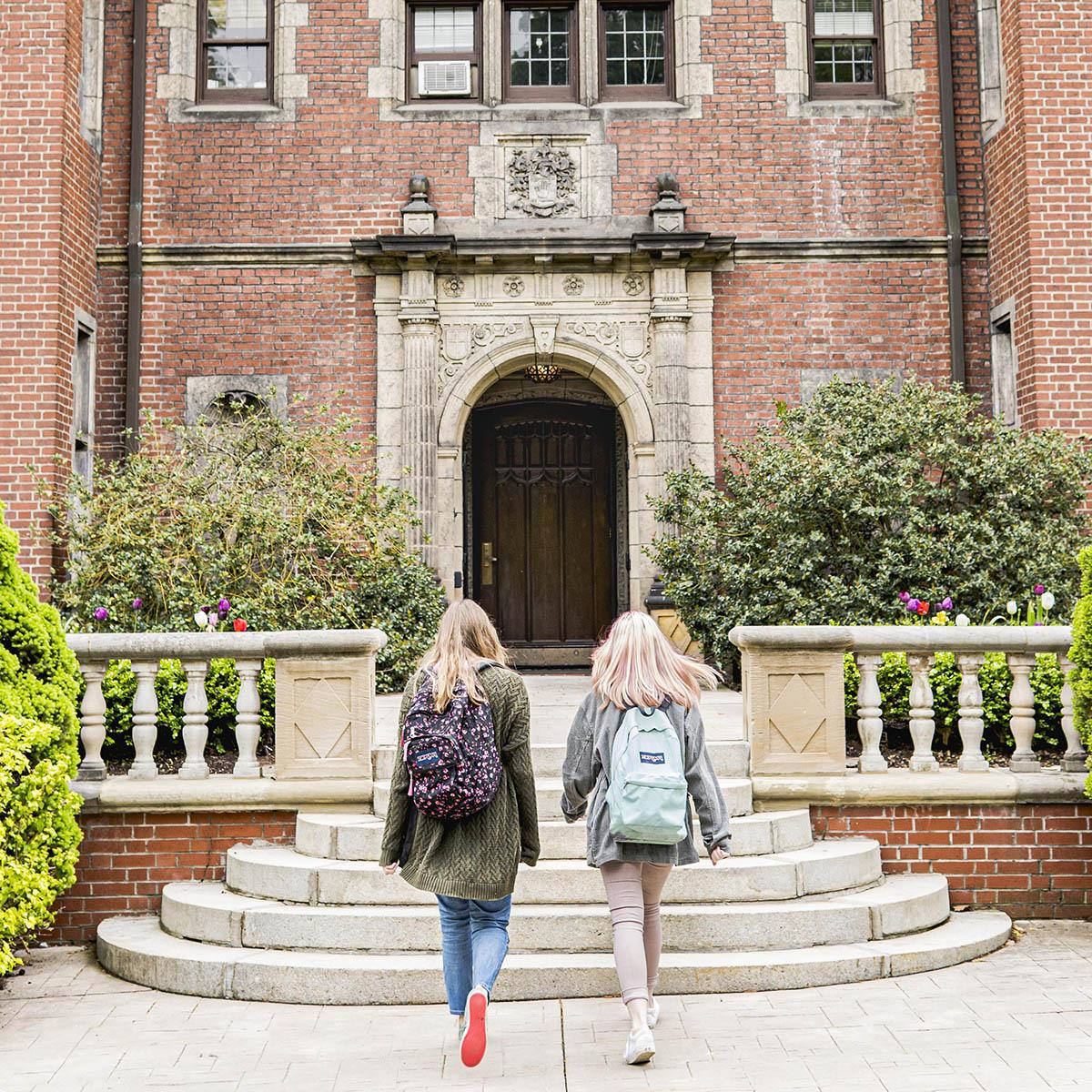 Photo of two young women with backpacks walking into a residence hall